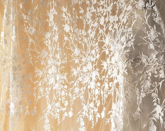 May include: White floral lace fabric with a delicate pattern of small flowers and branches. The lace is sheer and has a soft, flowing texture.