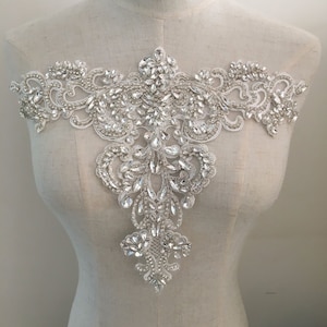 Può includere: Un'applicazione in pizzo bianco con un motivo floreale impreziosito da strass trasparenti. L'applicazione è perfetta per aggiungere un tocco di brillantezza agli abiti da sposa, agli accessori da sposa o ad altri capi per occasioni speciali.