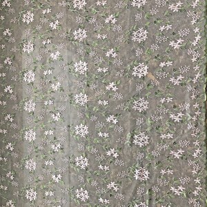 May include: White floral lace fabric with a delicate green vine pattern. The fabric has a sheer, lightweight texture.