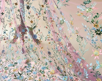May include: Sheer pink fabric with embroidered floral patterns. The embroidery features a variety of colorful flowers in shades of blue, yellow, green, and pink, with delicate green stems and leaves. The fabric is lightweight and flowing, ideal for apparel or decorative projects.