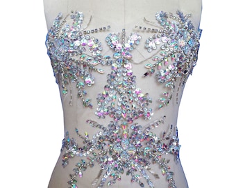 May include: A silver and iridescent rhinestone applique with a floral design. The applique is on a white fabric background.