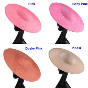 May include: Four wide-brimmed hats in shades of pink and beige are displayed. The hats are mounted on black mannequin heads. The colours include pink, baby pink, dusky pink, and khaki. The hats have a circular crown and a wide, flat brim.