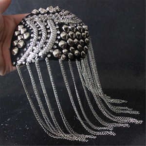 Pode incluir: Um acessório de cabelo de tecido preto com tachas de metal prateado e uma franja de correntes prateadas.