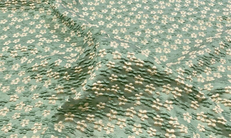 May include: A close-up of a textured fabric with a repeating pattern of small white flowers on a teal background.