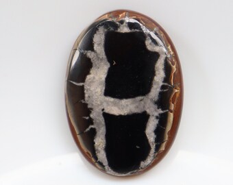 May include: A black and white agate cabochon with a unique pattern. The cabochon is oval shaped and has a smooth, polished surface.