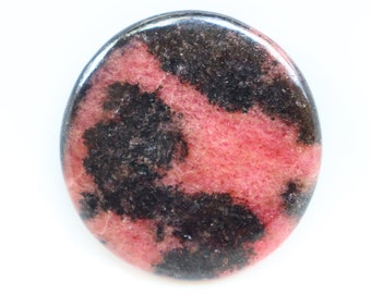 Puede incluir: Una piedra redonda y pulida con un patrón de mármol rosa y negro. La piedra es lisa y tiene un acabado brillante.