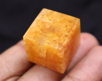 May include: A small, cube-shaped, orange crystal with a translucent, cloudy appearance.