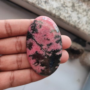 May include: A pink and black oval cabochon gemstone with a swirling pattern.