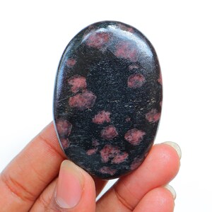 Peut inclure: Une pierre polie lisse de forme ovale avec une base noire et des taches roses et blanches.