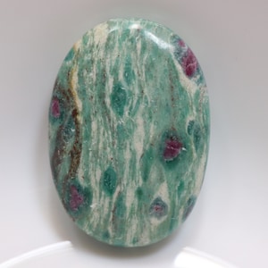 May include: An oval-shaped stone with a green and white pattern, featuring pink and brown inclusions. The stone is polished and smooth.