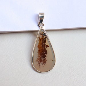 May include: A silver pendant featuring a teardrop-shaped stone with a brown and white dendritic agate pattern.