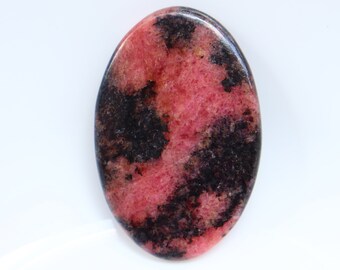 Puede incluir: Una piedra preciosa cabujón ovalada de color rosa y negro. La piedra tiene un patrón de remolino de rosa y negro.