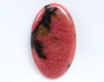Puede incluir: Gema ovalada pulida. La piedra presenta un color base rosa vibrante, acentuado por inclusiones negras y marrones oscuras. La gema se encuentra sobre un fondo blanco liso.
