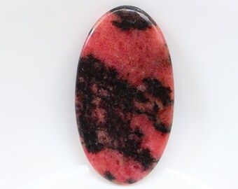 Puede incluir: Una piedra preciosa cabujón rosa y negra con un patrón de remolino. La piedra preciosa tiene forma ovalada y una superficie lisa y pulida.