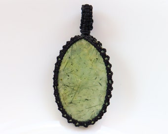 May include: A green oval stone pendant with black macrame knotting around the edge.