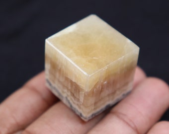 May include: A cube-shaped, light yellow calcite crystal with a layered, striated texture. The crystal is translucent and has a slight sheen.