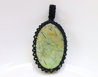May include: A green and gold oval-shaped gemstone pendant with black macrame cord. The gemstone has a unique pattern of inclusions.