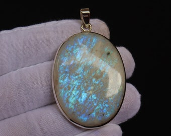 May include: A silver pendant with a large oval-shaped iridescent gemstone. The gemstone has a white base with blue and green iridescent flashes.