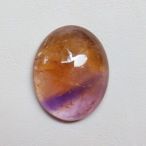May include: A smooth, oval-shaped gemstone with a gradient of colors, transitioning from a light brown to a deep purple.