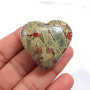 Può includere: Una pietra a forma di cuore con un motivo verde e rosso screziato. La pietra è lucidata e ha una superficie liscia.