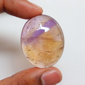 May include: A smooth, oval-shaped gemstone with a mix of purple and yellow hues. The stone has a translucent appearance, with swirls of color throughout.