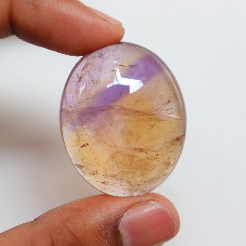 May include: A smooth, oval-shaped gemstone with a mix of purple and yellow hues. The stone has a translucent appearance, with swirls of color throughout.