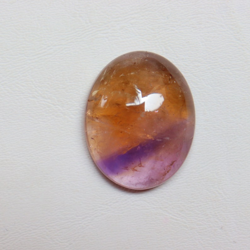 May include: A smooth, oval-shaped gemstone with a gradient of colors, transitioning from a light brown to a deep purple.