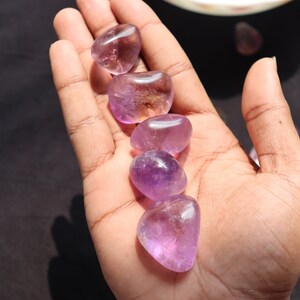 May include: Five smooth, polished amethyst stones in various shades of purple, arranged in a row on a hand.