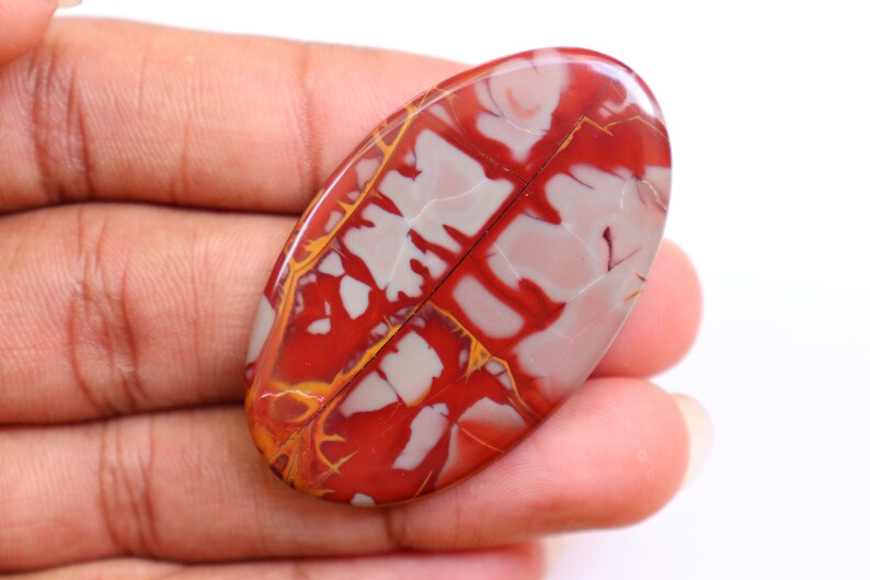 May include: Oval shaped red, white, and yellow jasper cabochon with a swirling pattern.
