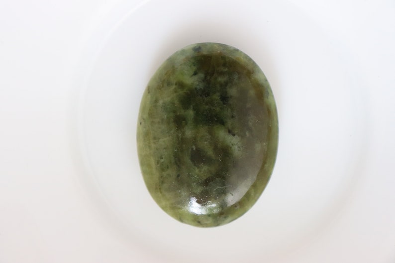 May include: A smooth, oval-shaped green stone with a mottled pattern. The stone has a polished finish and is a light green color.