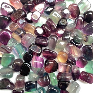 Könnte beinhalten: Eine Sammlung von geschliffenen Fluorit-Steinen in verschiedenen Schattierungen von Lila, Grün und Gelb. Die Steine sind glatt und poliert, mit einem glänzenden Finish.