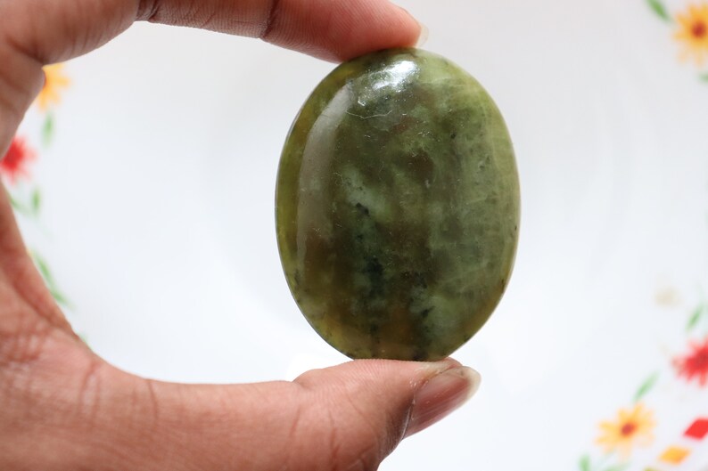 May include: A smooth, oval-shaped green stone with a mottled pattern. The stone is polished and has a glossy finish.