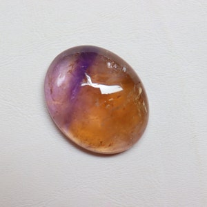 May include: A smooth, oval-shaped gemstone with a purple and orange color gradient. The gemstone is translucent and has a slight shimmer.