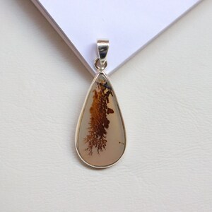 May include: A silver pendant featuring a teardrop-shaped dendritic agate stone with brown and white patterns.