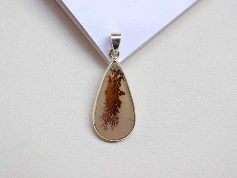 May include: A silver pendant featuring a teardrop-shaped dendritic agate stone with brown and white patterns.