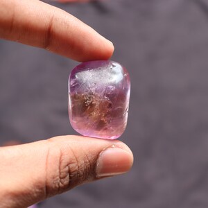 May include: A smooth, polished, purple and white gemstone with a cloudy, translucent appearance.