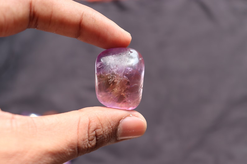 May include: A smooth, polished, purple and white gemstone with a cloudy, translucent appearance.