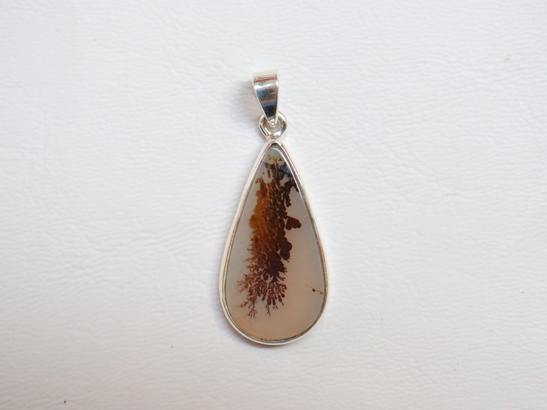 May include: A teardrop-shaped pendant with a silver setting and a brown and white agate stone. The agate has a dendritic pattern.