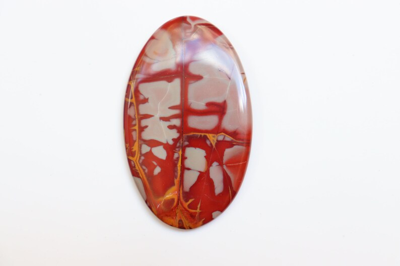 May include: A red, white, and yellow oval cabochon gemstone with a marbled pattern. The stone is polished and has a smooth surface.