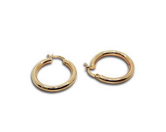 Puede incluir: Un par de pendientes de aro de oro de 14 quilates pulido con un diseño tubular liso y redondeado. Cada pendiente cuenta con un mecanismo de cierre de poste articulado seguro. El metal tiene un tono dorado cálido y brillante.