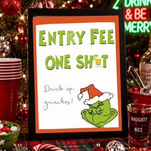 以下が含まれることがあります： オレンジ色の枠が付いた額入りの看板で、緑色の文字で「ENTRY FEE ONE SHOT」と書かれ、ショットグラスのアイコンがあります。その下には「Drink up, grinches!」という文字と、赤と白のサンタ帽子をかぶった緑色のキャラクターのイラストが描かれています。