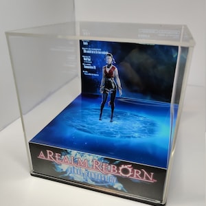 K&ouml;nnte beinhalten: Eine transparente Acryl-Vitrine mit einem Final Fantasy XIV-Diorama. Das Diorama zeigt eine Charakterfigur in roter und schwarzer Kleidung vor einem blau-wei&szlig;en Hintergrund. Der Sockel der Vitrine tr&auml;gt den Spieletitel "A Realm Reborn Final Fantasy XIV".