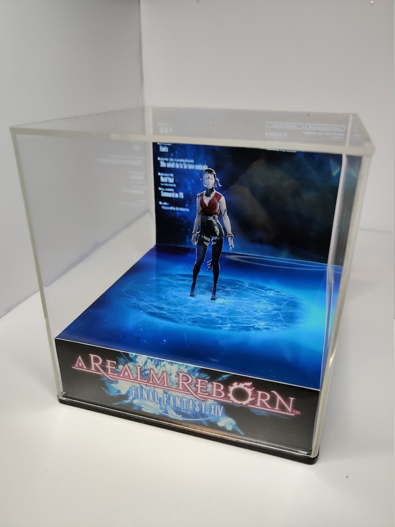 K&ouml;nnte beinhalten: Eine transparente Acryl-Vitrine mit einem Final Fantasy XIV-Diorama. Das Diorama zeigt eine Charakterfigur in roter und schwarzer Kleidung vor einem blau-wei&szlig;en Hintergrund. Der Sockel der Vitrine tr&auml;gt den Spieletitel "A Realm Reborn Final Fantasy XIV".