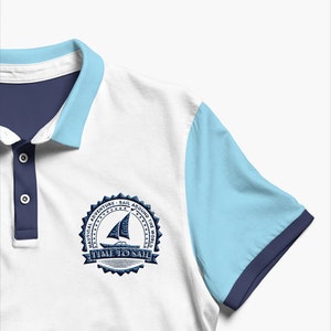 May include: White polo shirt with a blue and light blue color block design. The shirt has a navy blue collar and a navy blue embroidered patch on the left chest that says "Nautical Adventure - Sail Around The World - Time To Sail".