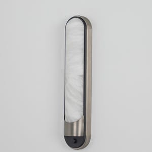 May include: A vertical wall sconce featuring a brushed nickel frame and a long, slender, white marbled glass diffuser. The fixture has a rounded top and a bottom section with a small black circular button, showcasing a clean, elongated design.