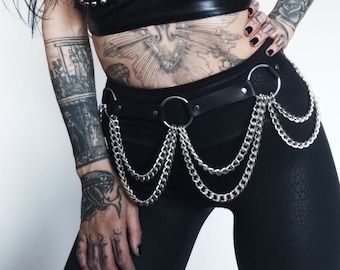 May include: A black leather halter top with silver studs, worn with black pants and a silver chain belt. The model has several tattoos on their arms and torso.