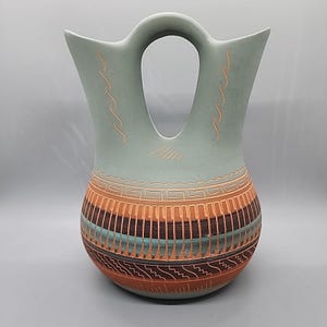 May include: A white ceramic mug with a black handle and the text "But First, Coffee" in a black, handwritten-style font. The mug is on a white surface.