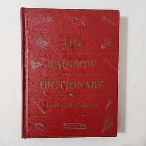 Puede incluir: Un libro de tapa dura rojo titulado "The Rainbow Dictionary" de Wendell W. Wright. La portada presenta ilustraciones de varios objetos, incluyendo un arcoíris, un paraguas, una pluma, un hacha, una concha, un pez, un cono y un paracaídas.