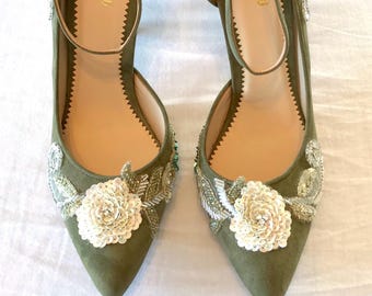 May include: A pair of olive green pointed-toe heels featuring an ankle strap and a beige insole with the text KYCHU printed in gold. The exterior is decorated with white sequined floral appliqués and silver beaded leaf-like embroidery.