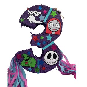 Puede incluir: Una pi&ntilde;ata con forma de n&uacute;mero tres de color morado decorada con estrellas brillantes y recortes de personajes que incluyen un perro fantasma blanco, una mujer de pelo rojo, un monstruo verde y una calavera blanca con tiras de papel.